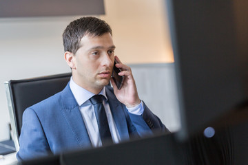 Wall Mural - Male stock broker talking on mobile phone while watching charts and data analyses on multiple computer screens.