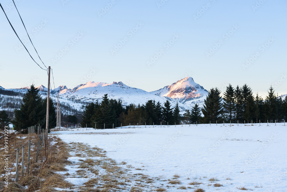 Snowy field surrounded by a fence with mountains in the background ...