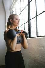 Confident Athlete Carrying Kettlebells While Standing By Window In Gym
