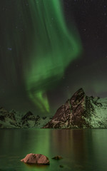 green northern lights (aurora borealis) over fjord with mountain in background