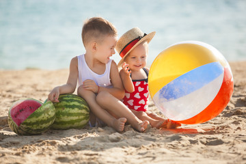 Wall Mural - Two little beautiful children on the beach with watermelons. Cute kids playing near the seaside smiling. Cheerful kids.