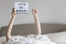 Female In Bed Under The Sheets Holding Up A Lets Go Monday Sign