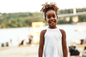 Portrait of little African-American girl. She's standing at the beach and smiling.