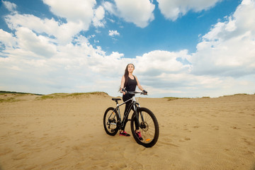 Wall Mural - Bicyclist at the summer sunset on the desert road in the reserve territory. Full length image of young female cyclist. Summer sunset. Bicycle and ecology lifestyle concept.