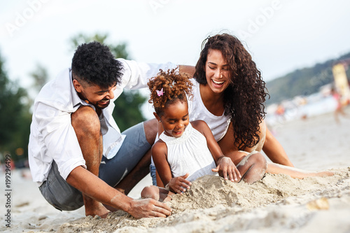 Fototapeta na szkło Młoda mieszana rasa rodzina siedzi i relaksuje na plaży w piękny letni dzień. Gra w piasku.