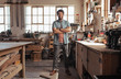 © mavoimages - Smiling young woodworker standing in his workshop full of tools