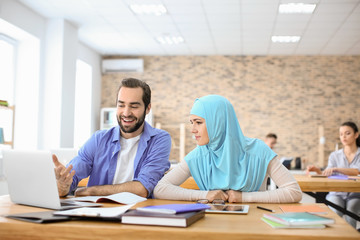 Canvas Print - Male student and his Muslim classmate using laptop in library