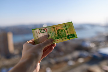 Banknote of new two hundred rubles in hand over city background.