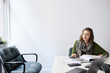 © Cavan Images - Businesswoman with book looking away while sitting at conference table in office