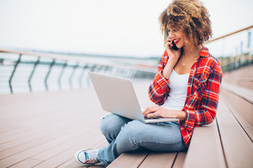 Young woman sitting at the stairs, working on laptop and talking on mobile phone 