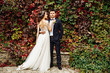 Beautiful bride in a wedding dress with bouquet and roses wreath posing with groom wearing wedding suit. Wedding day