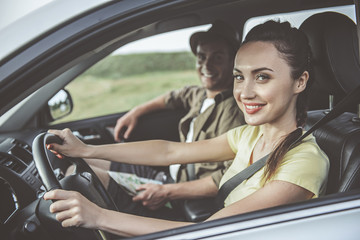 Our best adventure. Portrait of charming young woman is sitting in car with her boyfriend and smiling. She is driving and looking at camera happily. Selective focus