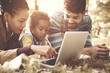© Mladen - Cheerful African American family lying down in park and using laptop.
