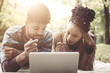 © Mladen - Young African American couple lying down in park and using laptop.