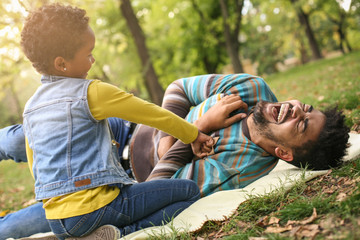 Canvas Print - Cheerful  African American little girl with her father in park playing together.