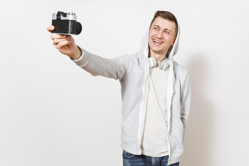 Young handsome smiling man student in t-shirt and light sweatshirt with hood with headphones photographs himself on retro camera isolated on white background. Concept of photography, hobby