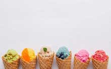 Various Of Ice Cream Flavor In Cones Blueberry ,strawberry ,pistachio ,almond ,orange And Cherry Setup On White Wooden Background . Summer And Sweet Menu Concept.