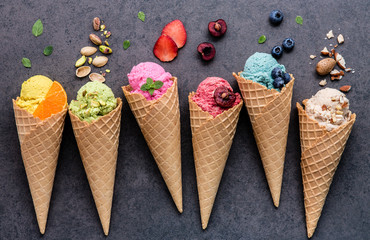 Fototapete - Various of ice cream flavor in cones blueberry ,strawberry ,pistachio ,almond ,orange and cherry setup on dark stone background . Summer and Sweet menu concept.