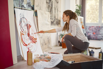 Artistic girl sitting in studio and paint on easel.