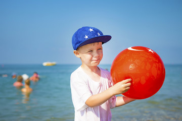 Portrait of boy on beach. Little boy in cap with an inflatable ball against the blue sea on clear, sunny summer day on vacation. Happy child smiling at sea. Playing children on sea beach.