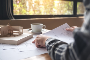 An architect working on an architecture model with shop drawing paper and coffee cup on table