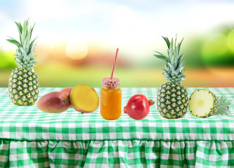 Healthy fresh tropical fruits composition on green white checkered tablecloth with bright colorful backround. Health concept. Diet concept. Glass filled with fresh pressed orange juice.