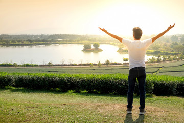 back view asian man two hand up in a green tea farm at sunset. concept of freedom and happy.