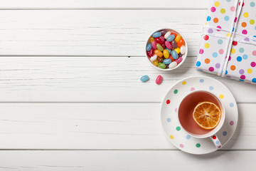 Gift box, cup of tea and colorful candies on white wooden background