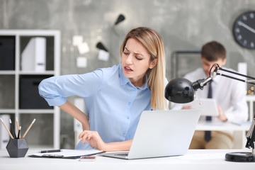 Wall Mural - Young woman suffering from back pain in office