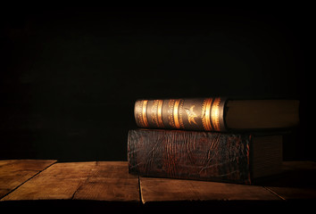 Wall Mural - image of stack of antique books over wooden table and dark background.