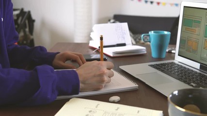 Freelancer's workplace. Web Developer makes sketches of the site in his notebook working remotely from home office