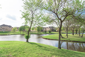 Wall Mural - Typical lakeside new-established community with newly built detached single-family homes. Cloud blue sky reflection near urban park with walking path in suburban Irving, Texas, USA