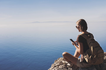 Wall Mural - Young traveler woman on a hiking trail using smartphone, travel and active lifestyle concept