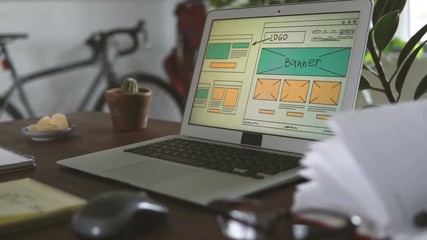 Freelancer's workplace. Web Developer makes sketches of the site in his notebook working remotely from home office