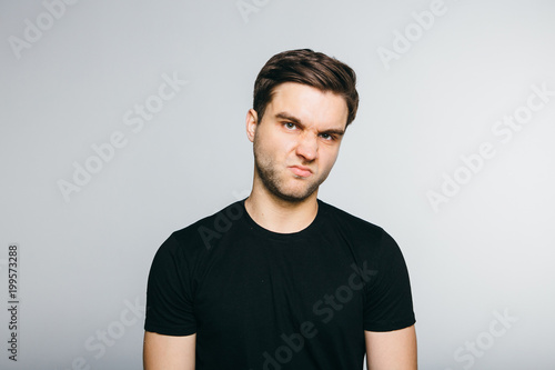 Man disgust while standing against grey background. Tableau sur Toile