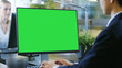 © Gorodenkoff - In the Office Businessman works at His Desk on a Personal Computer with Mock-up Green Screen. His Colleague Sets Opposite to Him.