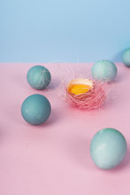 Several Blue Eggs And Yolk In Egg Shell Decorated With Nest Of Pink Sisal On The Minimalist Pink And Blue Background.