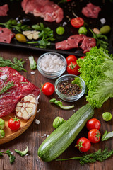 Wall Mural - Flat lay of raw beefsteak with vegetables, herbs and spicies on metal tray, close-up, selective focus