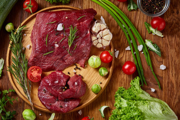 Wall Mural - Still life of raw beef meat with vegetables on wooden plate over white background, top view, selective focus