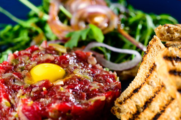 Wall Mural - Dish with beef tartare, tomatoes and leaves in a cafe, close-up