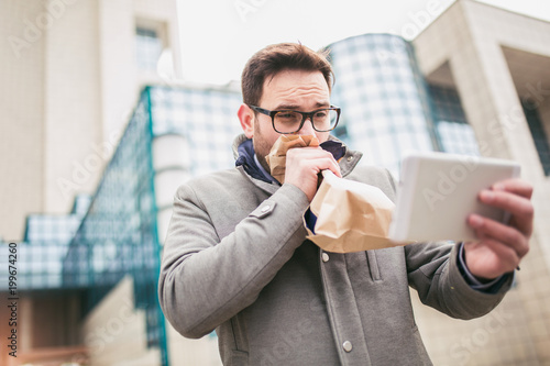 Cuadros en Lienzo Businessman holding paper bag over mouth as if having a panic attack and looking in digital tablet