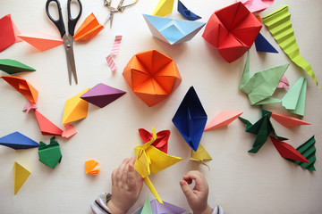 the child makes origami. multicolored origami and paper on a white table. origami lesson