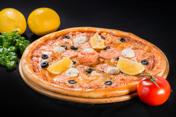 Canvas Print - Delicious juicy pizza with salmon, lemon and olives on wooden board on dark background