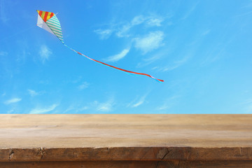 Wall Mural - Image of empty rustic table in front of Colorful kite flying in the blue sky through the clouds. For product display presentation.