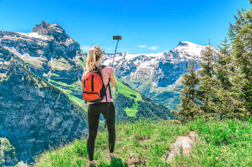 Wall Mural - woman traveler photographing herself, making a salfi on the smartphone, against the backdrop of the mountain peaks of Switzerland