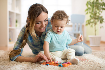 Wall Mural - Mother is teaching child son how to play xylophone toy