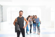 © uv_group - Portrait of handsome sportive yoga teacher men holding exercise mat while practicing yoga at the gym studio with background of his team