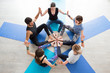 © uv_group - Group of sporty happy people sitting on the gym floor at yoga mat in a circle together, resting and meditating after yoga class with instructor indoors. Healthy lifestyle concept