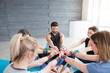 © uv_group - Group of sporty happy people sitting on the gym floor at yoga mat in a circle together, resting and meditating after yoga class with instructor indoors. Healthy lifestyle concept