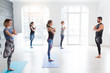 Yoga men instructor teaches group of people, fitness, sport and healthy lifestyle concept. Young women with personal trainer doing yoga exercises on mat in gym studio